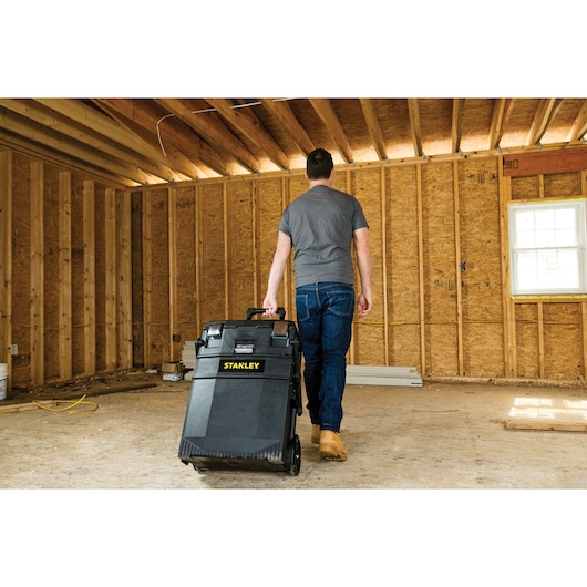 Photo of STANLEY 020800R rolling tool box being pulled by a person in an unfinished wooden room.