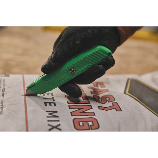 Stanley 10-179 green utility knife cutting open concrete mix bag, close-up, held with black work glove.