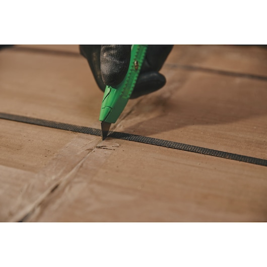 Photo of STANLEY 10-179 utility knife cutting cardboard box, close-up view of green handle and gloved hand.