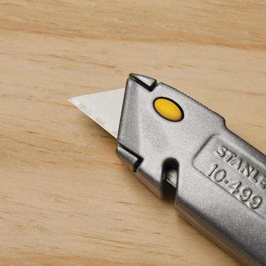 Photo of STANLEY 10-499 utility knife with a sharp blade and yellow button, close-up on wood surface.