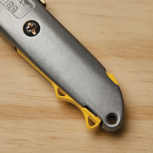 Photo of STANLEY 10-499 utility knife handle in silver and yellow, close-up side angle on wood surface.
