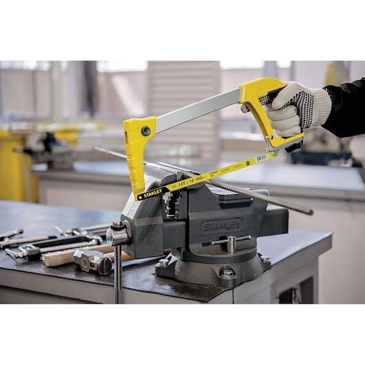 Stanley 15-098 hacksaw with yellow handle cutting metal rod in workshop, close-up side angle.
