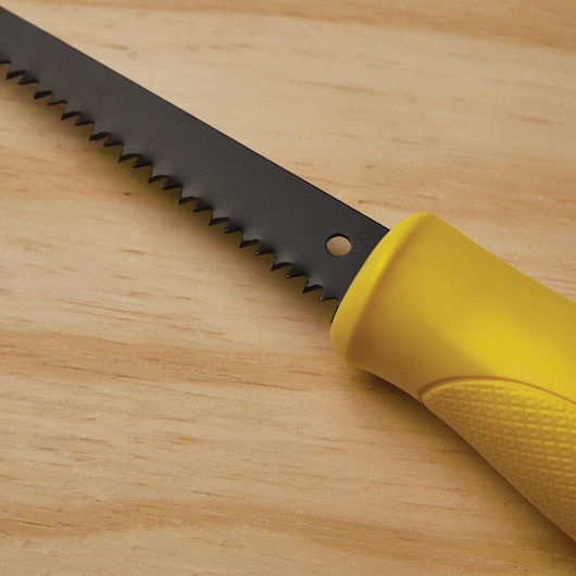 STANLEY 15-556 saw with yellow textured handle and black serrated blade, close-up view on wood surface.
