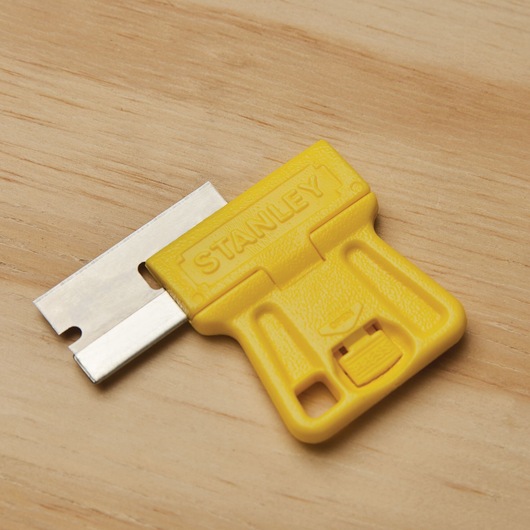 STANLEY 28-100 yellow plastic scraper with metal blade on a wood surface, close-up angle.