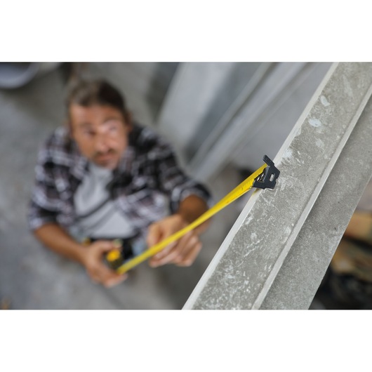 STANLEY 30-626 tape measure in use, yellow tape extended along a metal beam, side angle photography.