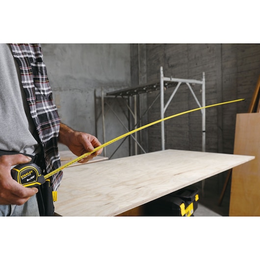 STANLEY 30-626 tape measure being used to measure plywood sheet in a workshop, view focused on tool and tape.