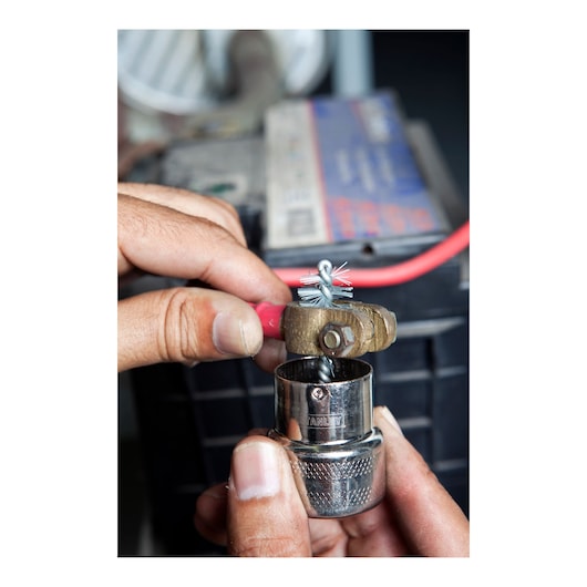Photo of STANLEY 79-047 socket held in hand, close-up view with metallic wire brush and battery in background.