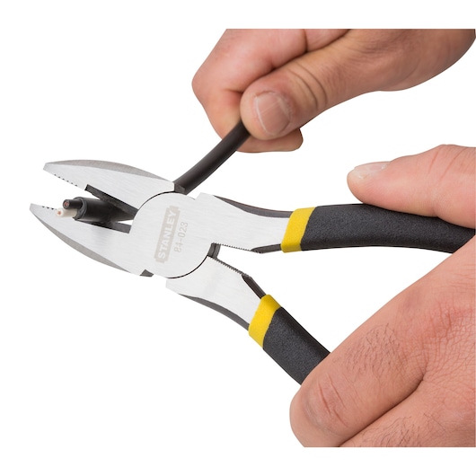 STANLEY 90-162LA lineman pliers with black and yellow handle cutting a black electrical wire, close-up.