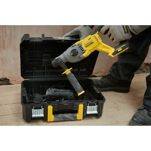 STANLEY SBH900M2K-B3 rotary hammer held above open black and yellow case on a construction site.