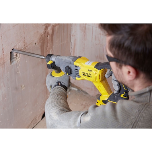 STANLEY SBH900M2K-B3 rotary hammer in use drilling into wall, yellow and black tool held by gloved hand.