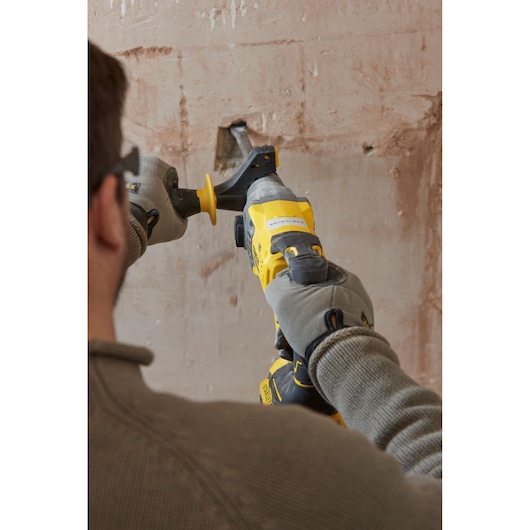 Stanley SBH900M2K-B3 rotary hammer used on a plaster wall, rear view, person wearing gloves.