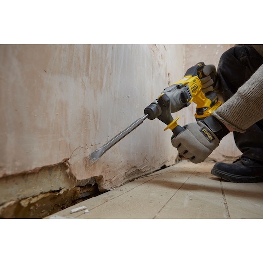 Stanley SBH900M2K-B3 rotary hammer drill in use chiseling wall, close-up, construction setting.