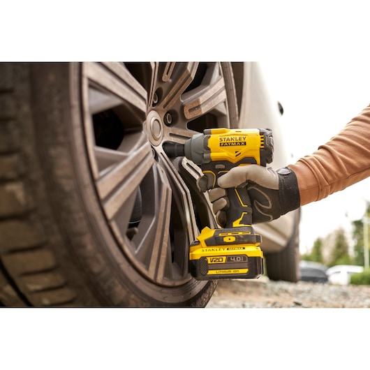 STANLEY SBW920M2K cordless impact wrench used on car wheel, close-up side angle, yellow and black tool.