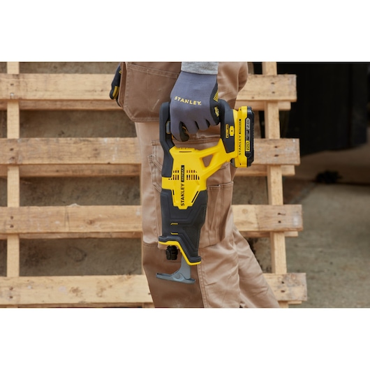 STANLEY SCR300D2K cordless reciprocating saw held by worker in brown pants, outdoor construction setting.