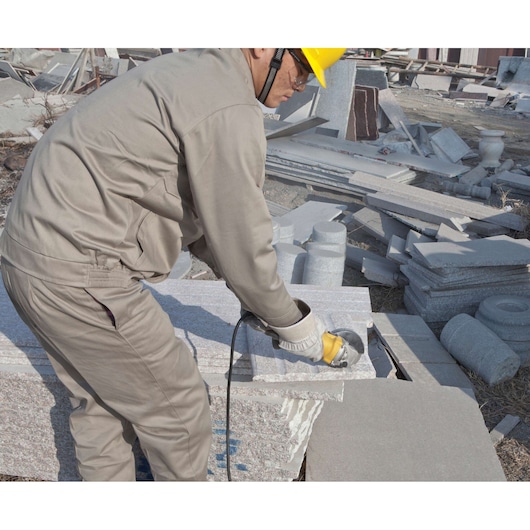 STANLEY SGS1045K angle grinder in use, worker cutting stone slab outdoors, close-up side view.