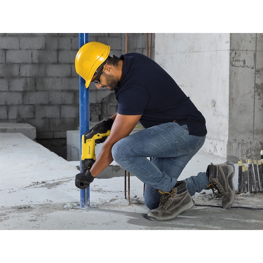 STANLEY SHR263K-BR rotary hammer drill in use on wood, worker wearing yellow hard hat and black uniform.