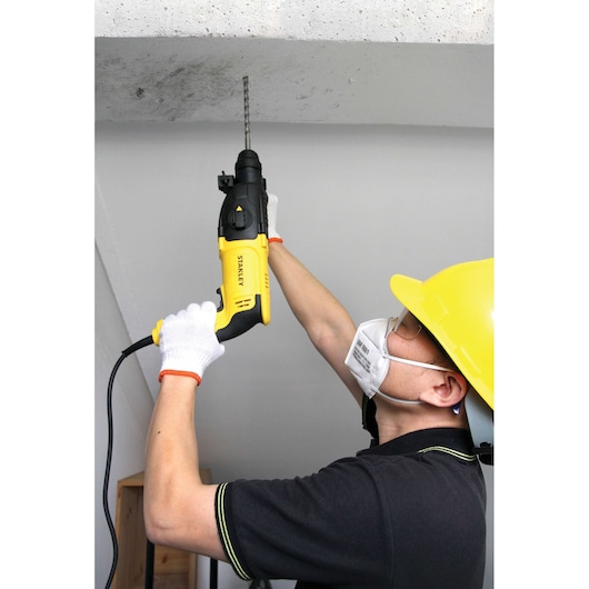 Stanley SHR263K-BR rotary hammer drill in use, yellow and black, drilling concrete ceiling.