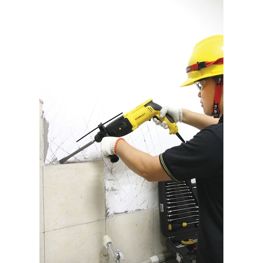 STANLEY SHR263K-BR rotary hammer used by worker with gloves and helmet to remove tiles, tool case visible in background.