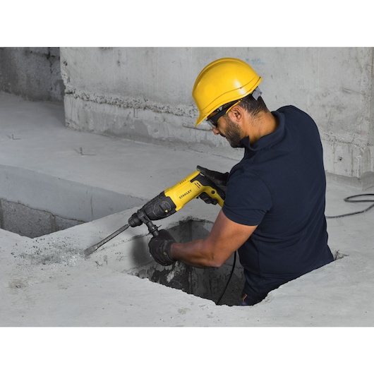 Photo of STANLEY SHR263K-BR rotary hammer drill in use on concrete, operated by a worker in safety gear.