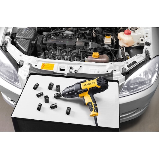 STANLEY SIW901-B2 impact wrench with sockets shown on a table in front of an open car engine, front angle.