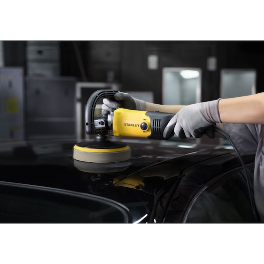 Stanley SP137 yellow and black polisher in use on car roof, held by gloved hands in workshop setting.