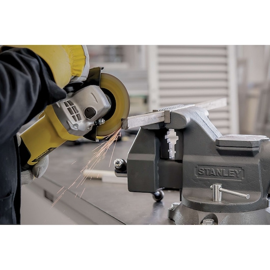 Photo of STANLEY STA8061 bench vise holding metal bar, with angle grinder cutting and producing sparks.