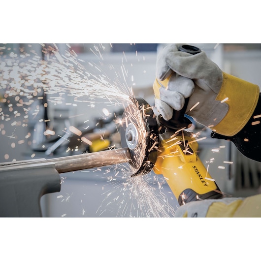 Photo of STANLEY STA8061 angle grinder in use, with sparks flying while cutting metal pipe, close-up action shot.