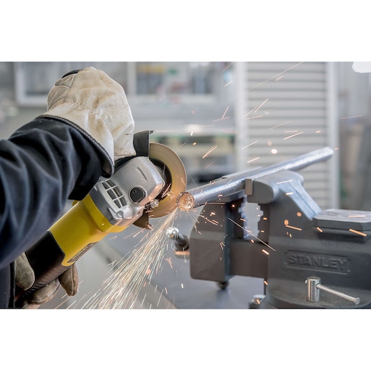 Photo of STANLEY STA8061 grinder in use cutting metal pipe held by vise, visible sparks, close-up action shot.