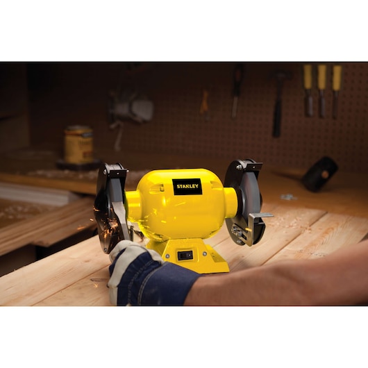 STANLEY STGB3715 bench grinder, yellow, used on a wooden workbench with sparks, side angle.