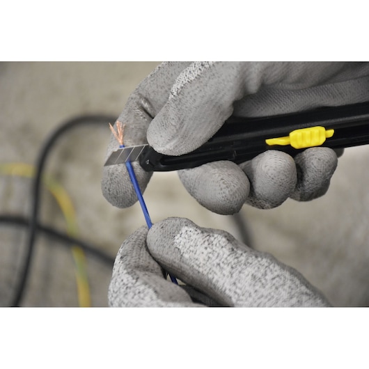 Photo of STANLEY STHT10322 utility knife cutting blue wire, gray gloves visible, close-up view.
