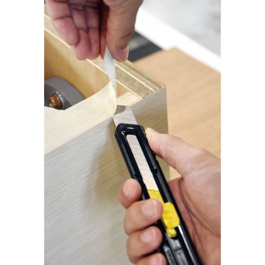 STANLEY STHT10323-840 utility knife cutting tape on wood, close-up angle.