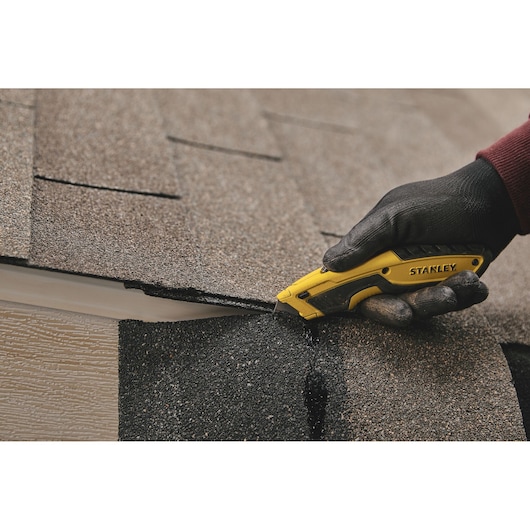 STANLEY STHT10479 utility knife cutting roofing shingles, close-up of tool in use.