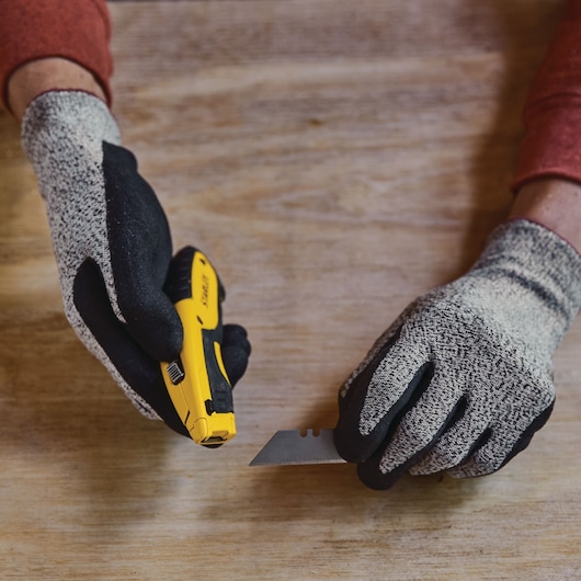 STANLEY STHT10479 utility knife and blade held by gloved hands on a wooden surface, close-up.