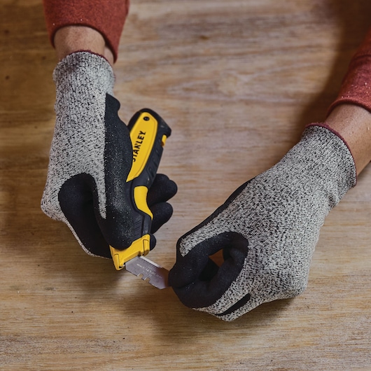 STANLEY STHT10479 utility knife held by gloved hands, blade being changed on wooden surface.