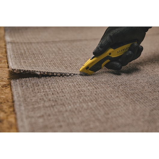 Stanley STHT10479 utility knife cutting carpet, close-up photography.
