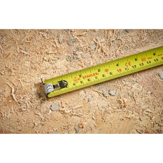 Stanley STHT37235-5 yellow tape measure on wood surface with sawdust and debris.