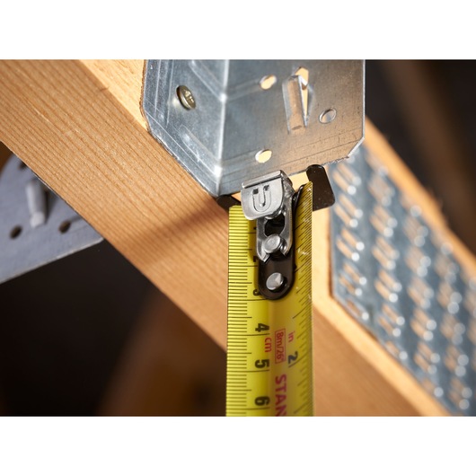 STANLEY STHT37236-5 tape measure close-up measuring wooden beam with metal bracket, yellow blade visible.