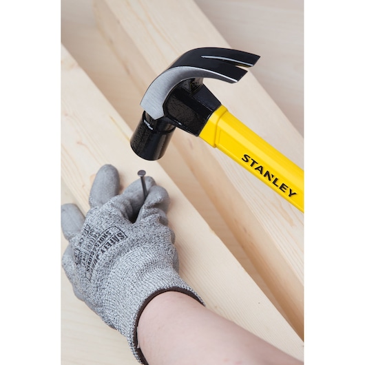 Stanley STHT51391 claw hammer with yellow handle used to drive nail into wood, close-up photo.