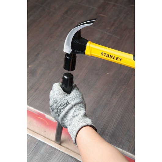 Photo of STANLEY STHT51391 claw hammer with yellow handle in use, striking a black post, person's gloved hand holding post.