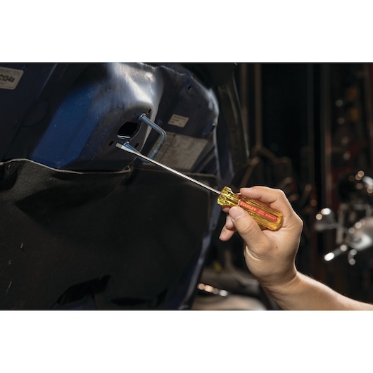 STANLEY STHT69112 screwdriver with yellow handle being used on a car interior bolt, side view.