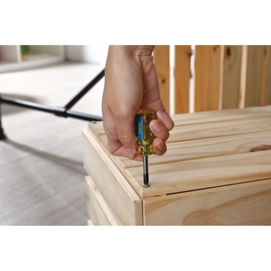 Photo of a hand using a STANLEY STHT69144 screwdriver to fasten a screw on a wooden crate.