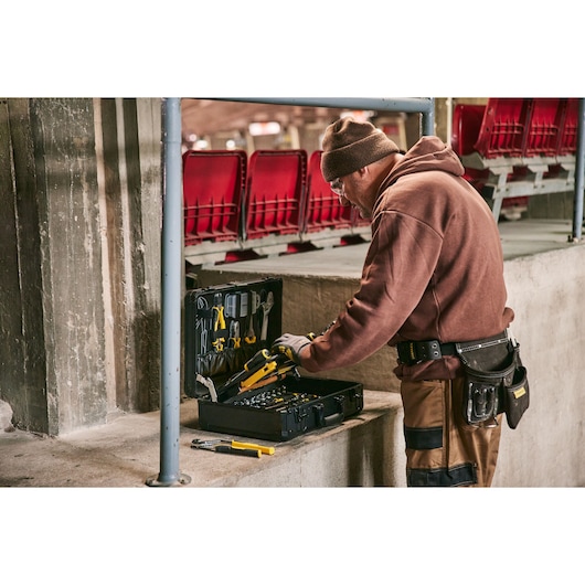 STANLEY STMT98109-LA tool set in open case used by worker in brown hoodie, with red seats in background, side view.