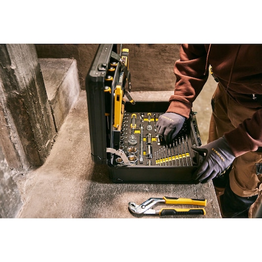 STANLEY STMT98109-LA tool set in black case, assorted tools, worker using set, photography on concrete surface.