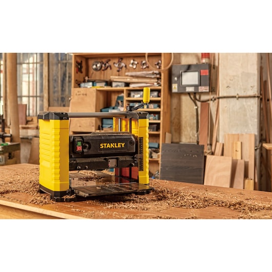 Stanley STP18-B2 planer in workshop, yellow and black, surrounded by wood shavings on workbench.