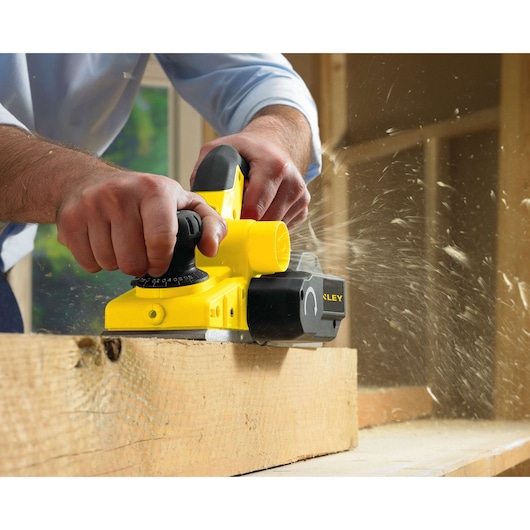 Stanley STPP7502-B2 electric planer being used on wood, close-up photography, yellow and black tool.
