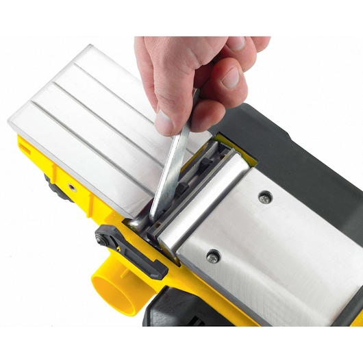 STANLEY STPP7502-B2 planer close-up, hand adjusting blade with tool, silver and yellow design, top view.