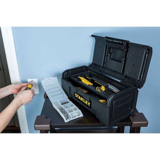 STANLEY STST16420 black toolbox with yellow handle, open to show tools inside, on a table next to hardware organizer.