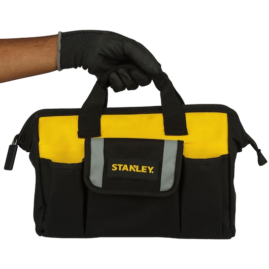 Stanley black and yellow tool bag held by a gloved hand, featuring multiple pockets and a zippered top.